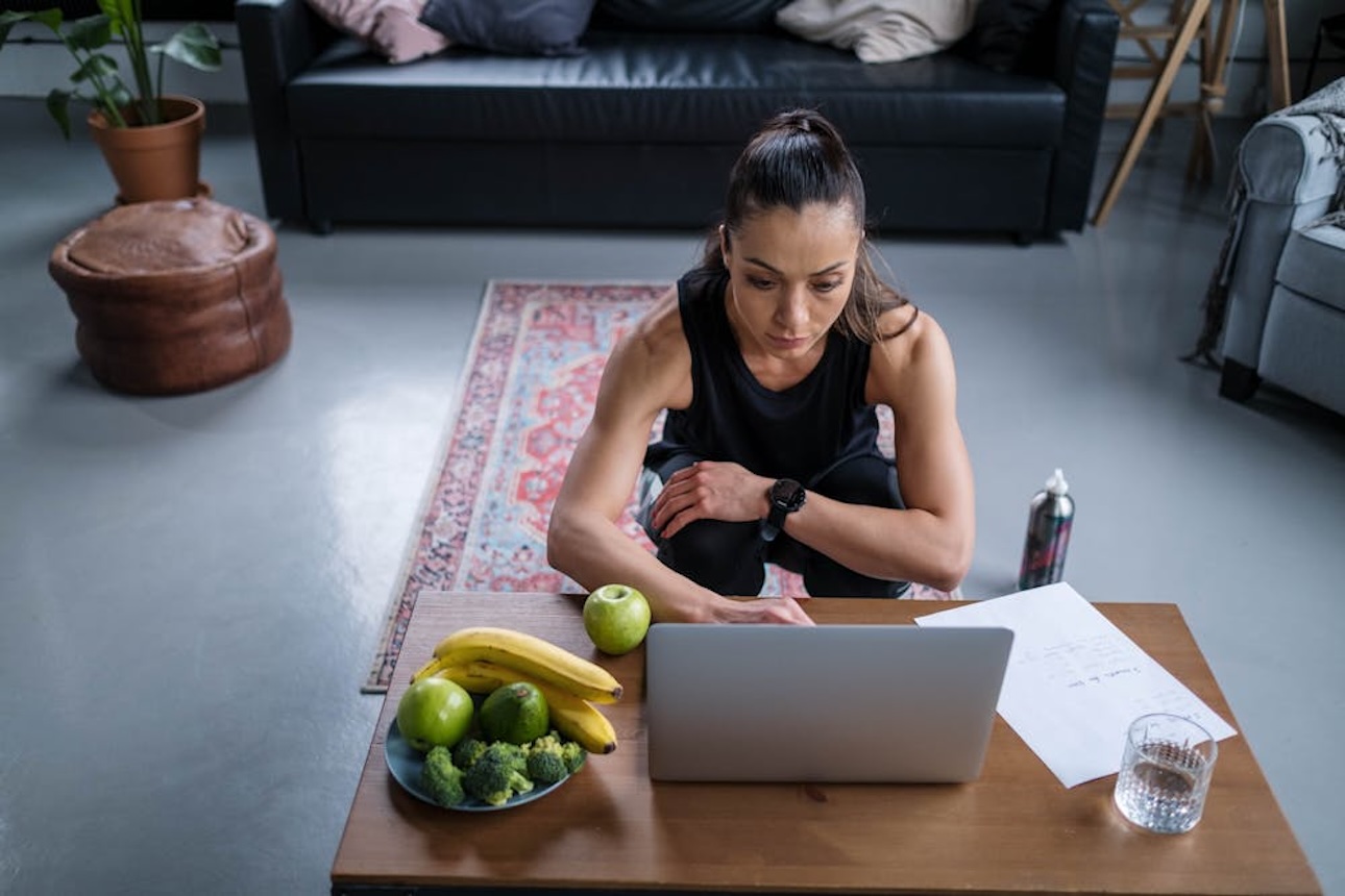 Fit woman working from laptop at home while in a deep squat position.