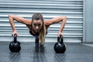 Muscular woman doing pushups with kettlebells